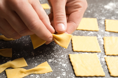 Woman making farfalle pasta at grey table, closeup