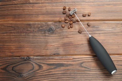 Black milk frother wand and coffee beans on wooden table, top view. Space for text