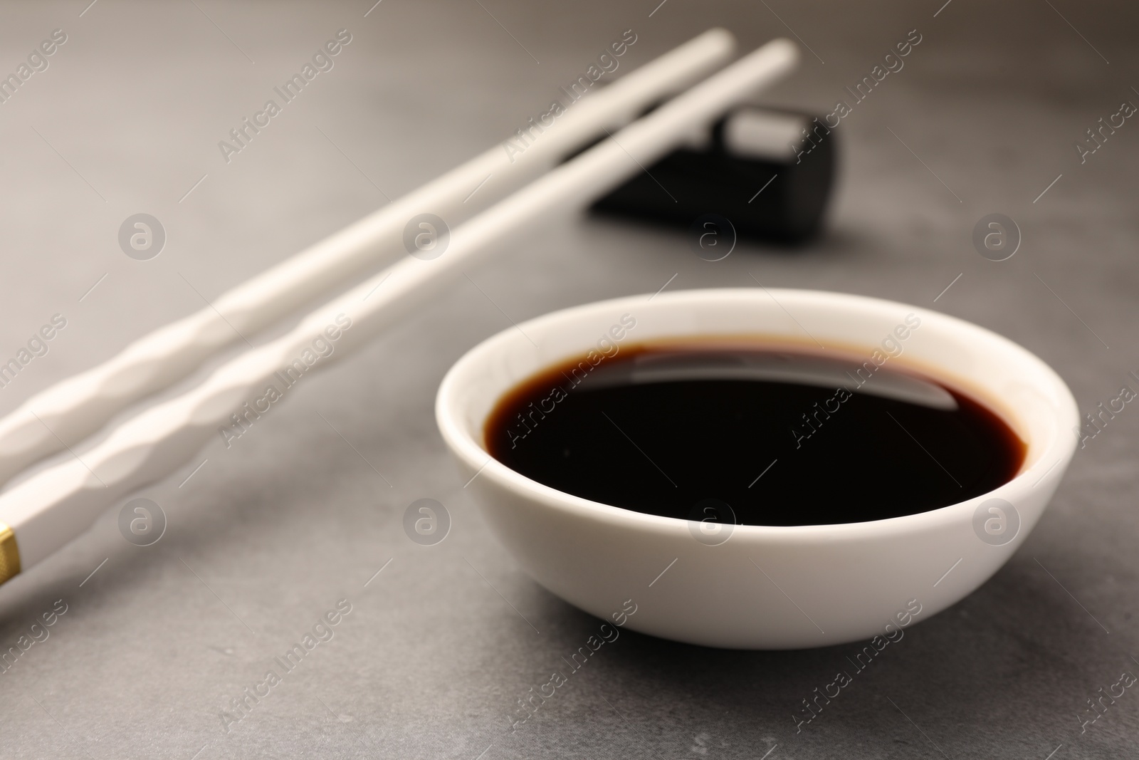 Photo of Bowl with soy sauce and chopsticks on grey table, closeup