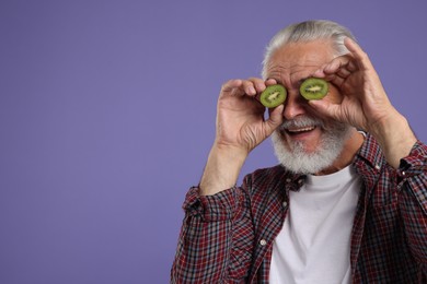 Photo of Senior man covering eyes with halves of kiwi on purple background, space for text
