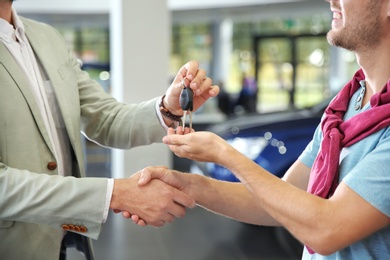 Photo of Salesman shaking hands with customer while giving car keys in auto dealership, closeup