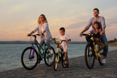 Photo of Happy family with children riding bicycles near river at sunset