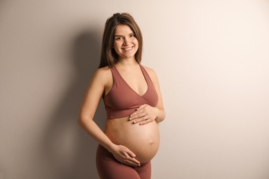 Photo of Pregnant young woman touching belly on beige background