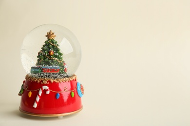 Photo of Beautiful snow globe with Christmas tree on beige background, space for text