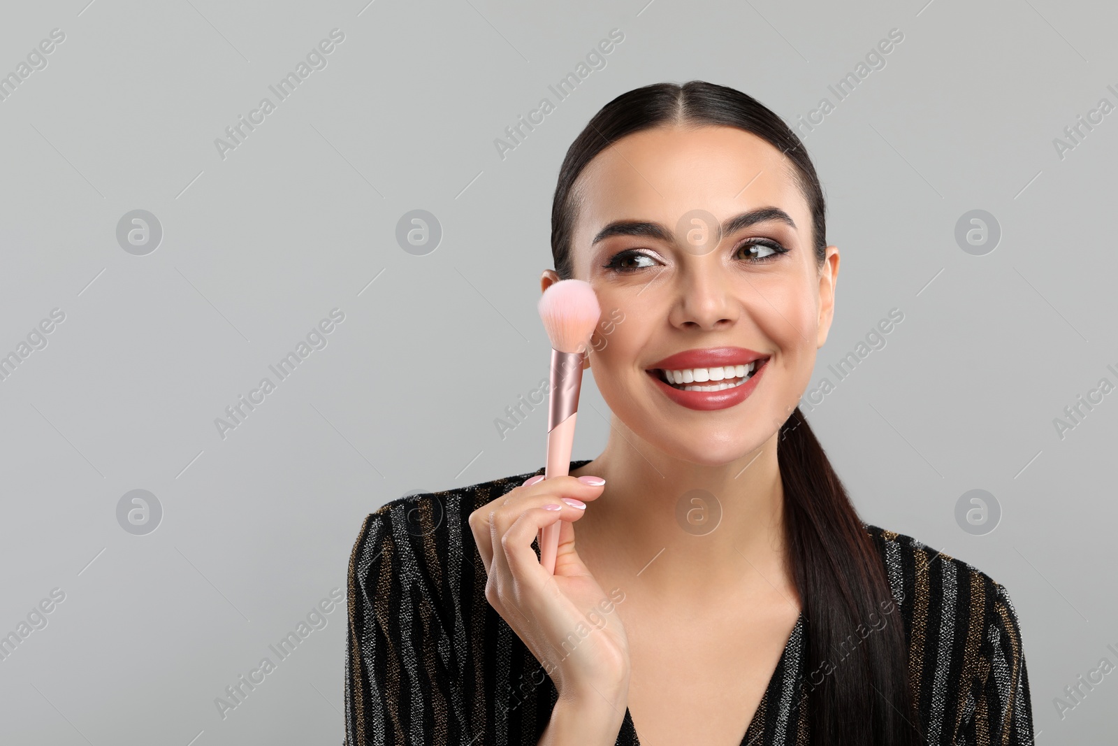 Photo of Everyday makeup. Beautiful woman applying face powder on light grey background, space for text