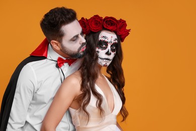 Couple in scary bride and vampire costumes on orange background, space for text. Halloween celebration