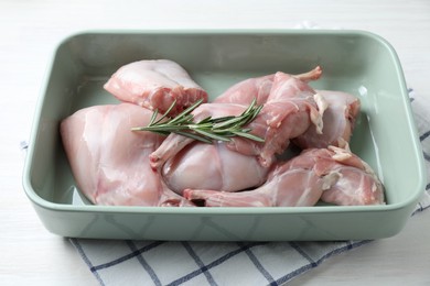 Photo of Raw rabbit meat and rosemary in baking dish on white wooden table, closeup