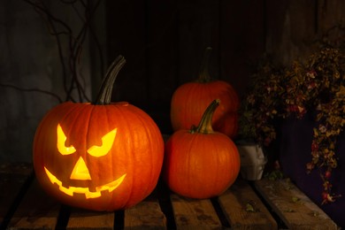 Scary jack o'lantern pumpkin on wooden bench in darkness. Halloween decor
