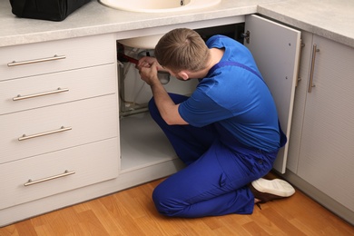 Photo of Professional plumber in uniform fixing kitchen sink