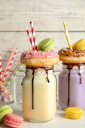 Photo of Mason jars with delicious milk shakes and macaroons on table