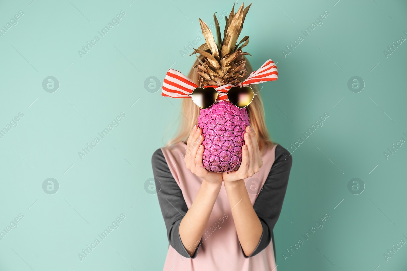 Photo of Woman holding pineapple with sunglasses and ribbon on color background