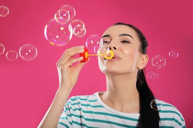 Young woman blowing soap bubbles on pink background