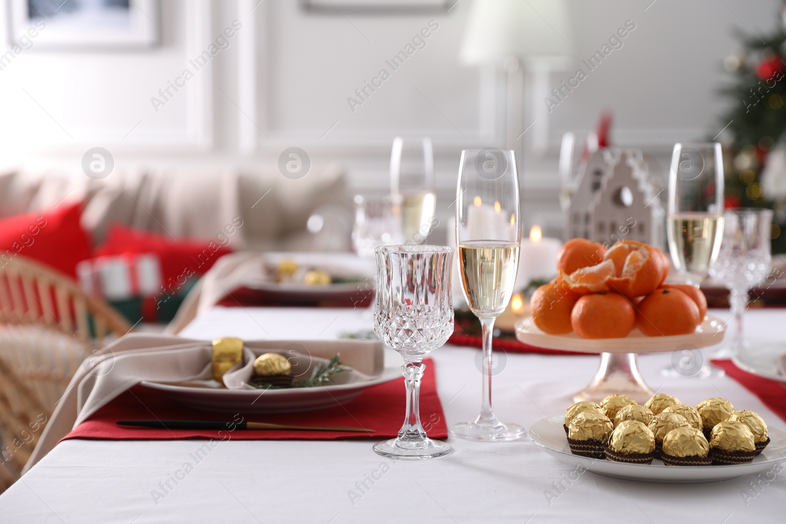 Photo of Christmas table setting with tangerines, candies and dishware indoors