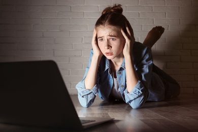 Photo of Shocked teenage girl with laptop on floor in dark room. Danger of internet