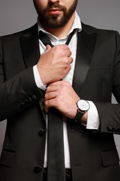 Photo of Bearded man tightening tie on grey background, closeup