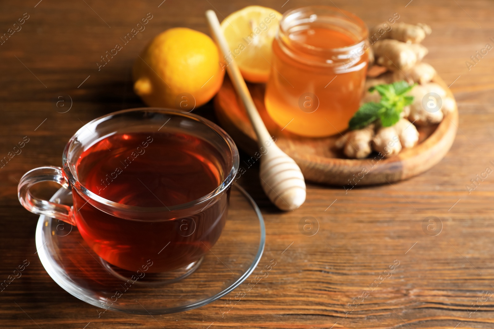 Photo of Cup of delicious ginger tea and ingredients on wooden table