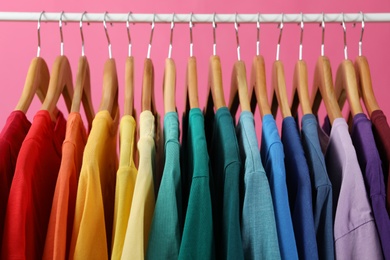 Rack with bright clothes on pink background. Rainbow colors