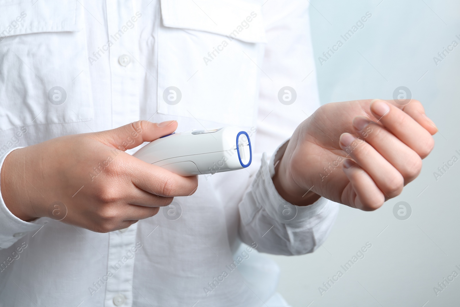 Photo of Woman measuring temperature with non contact infrared thermometer on light background, closeup