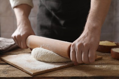 Photo of Man rolling raw dough at wooden table, closeup