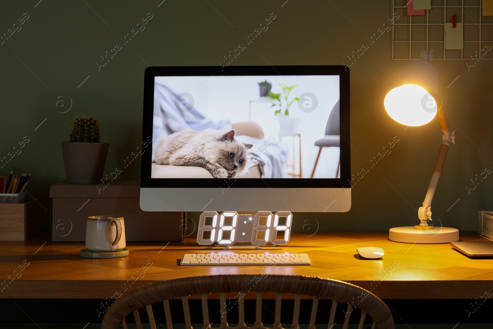 Photo of Stylish workplace with computer, houseplant and lamp near olive wall at home