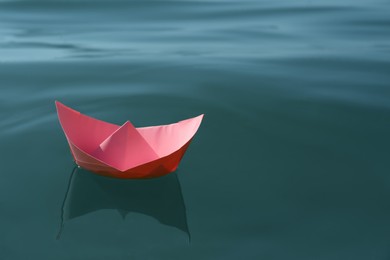 Photo of Pink paper boat floating on water surface, space for text