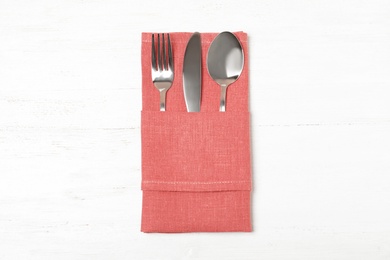 Photo of Folded napkin with fork, spoon and knife on white wooden background, top view