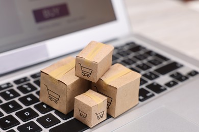 Image of Internet store. Small cardboard boxes with shopping carts on laptop, closeup