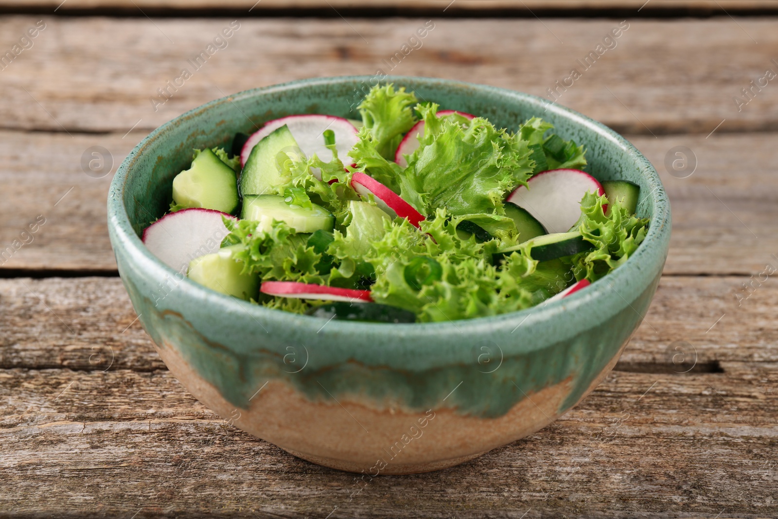 Photo of Delicious salad with radish, lettuce and cucumbers in bowl on wooden table, closeup