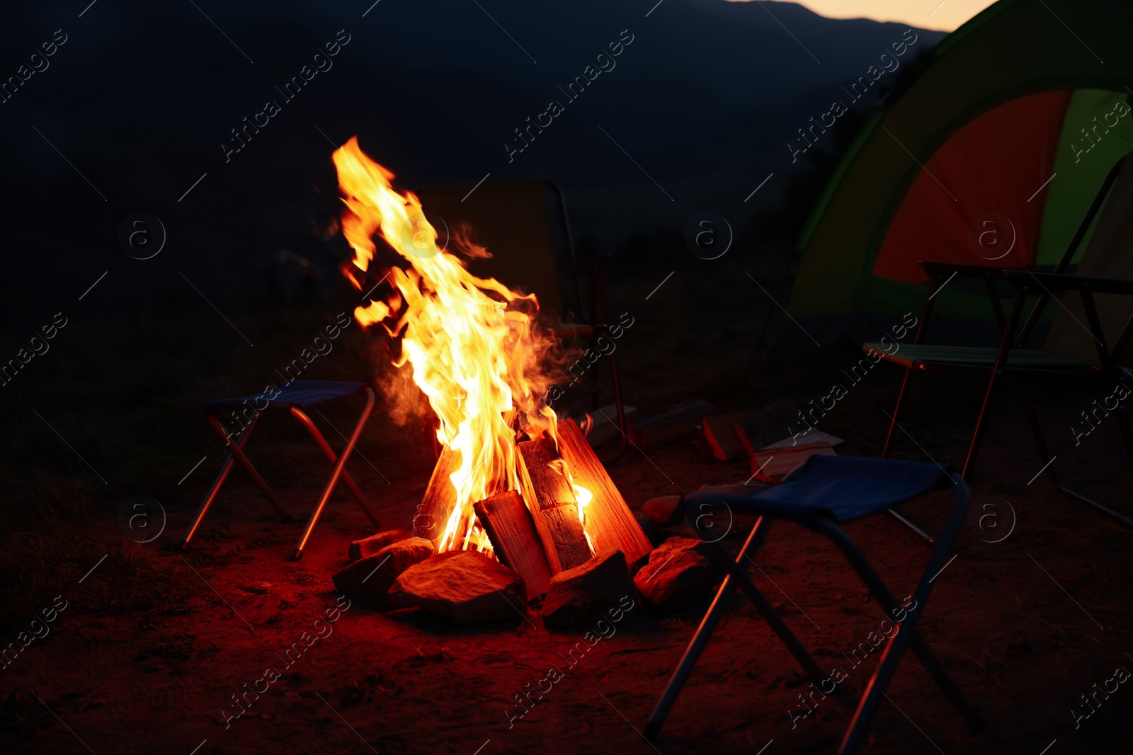 Photo of Beautiful bonfire and folding chairs near camping tent outdoors in evening