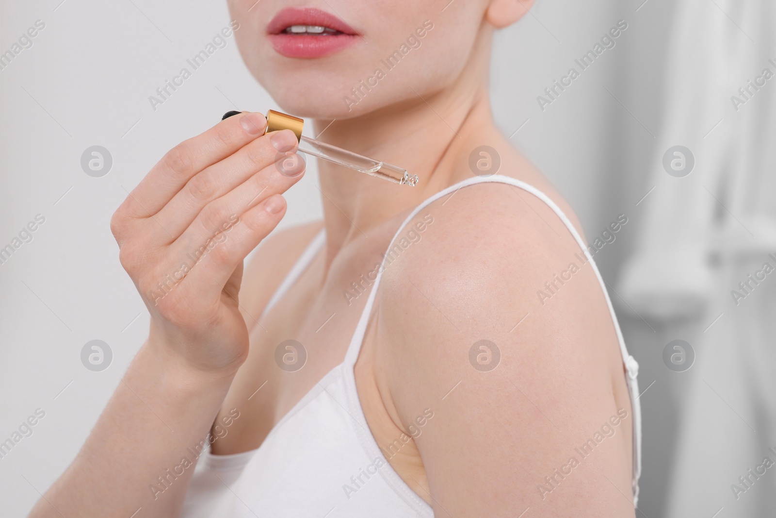 Photo of Woman applying essential oil onto shoulder in bathroom, closeup