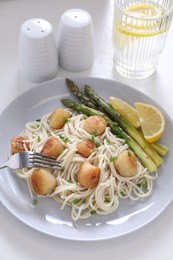 Photo of Delicious scallop pasta with asparagus, green onion and lemon served on white table, closeup
