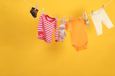 Photo of Different baby clothes and toys drying on laundry line against orange background. Space for text