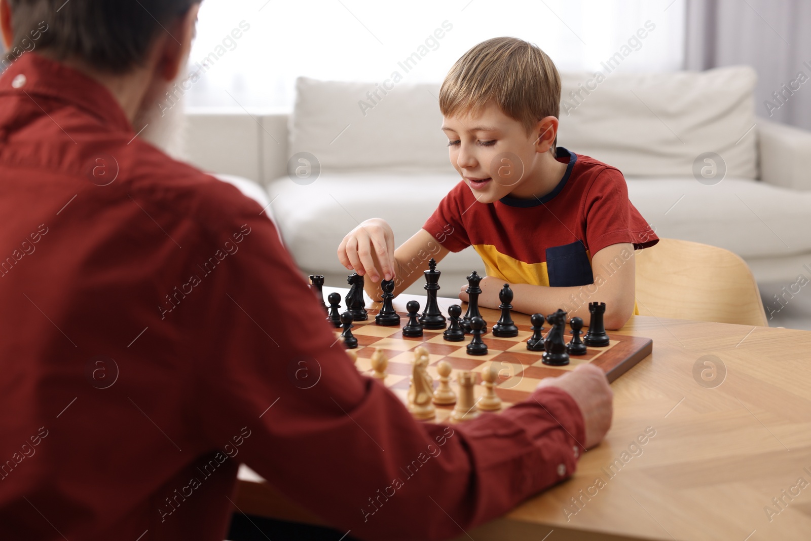 Photo of Little boy playing chess with his grandfather at table in room