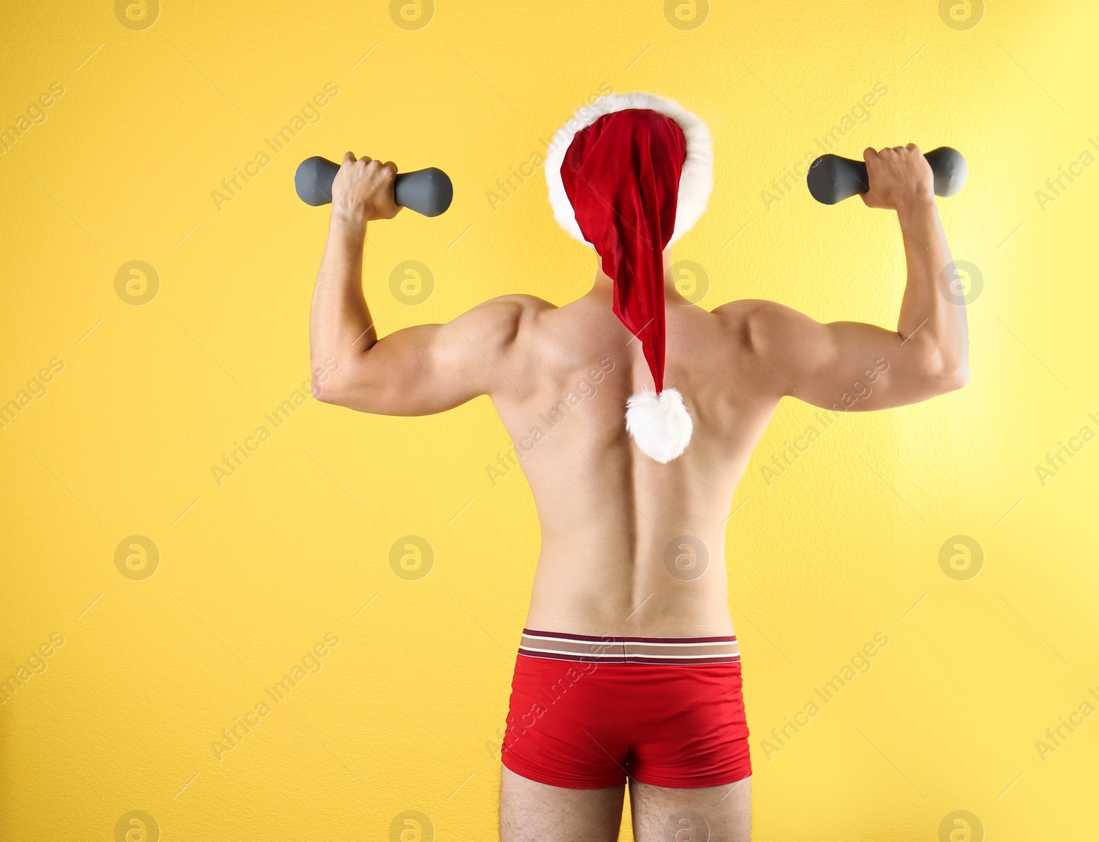 Photo of Shirtless sexy young Santa Claus with dumbbells on color background