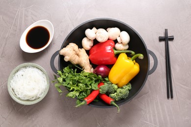 Photo of Wok, chopsticks and different products on grey textured table, flat lay