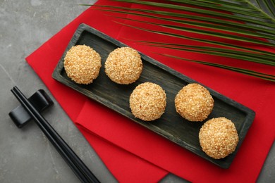 Photo of Delicious sesame balls, green leaf and chopsticks on grey table, flat lay