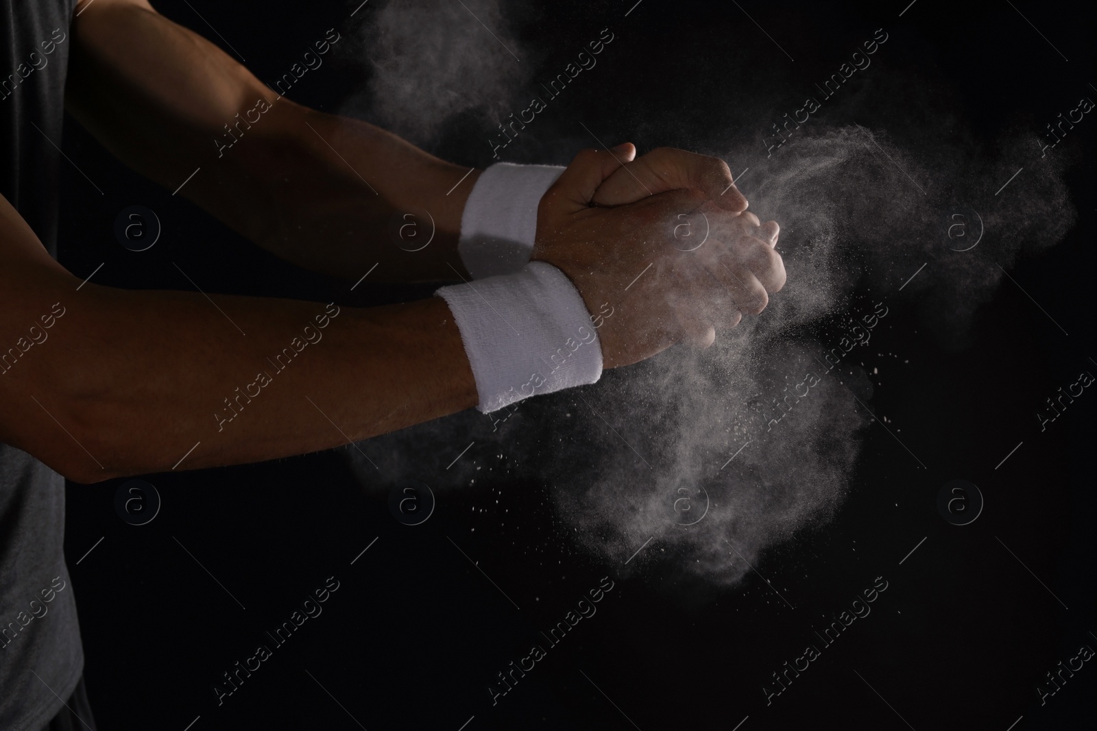 Photo of Young man applying chalk powder on hands against dark background