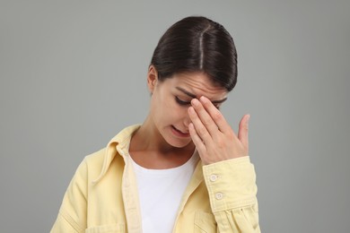 Embarrassed young woman covering face with hand on grey background