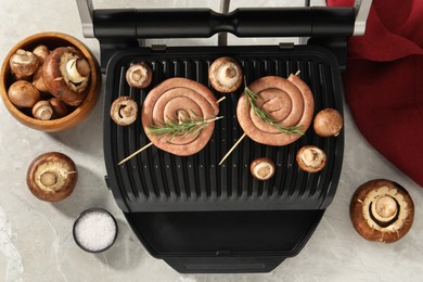 Photo of Electric grill with homemade sausages, rosemary and mushrooms on marble table, flat lay