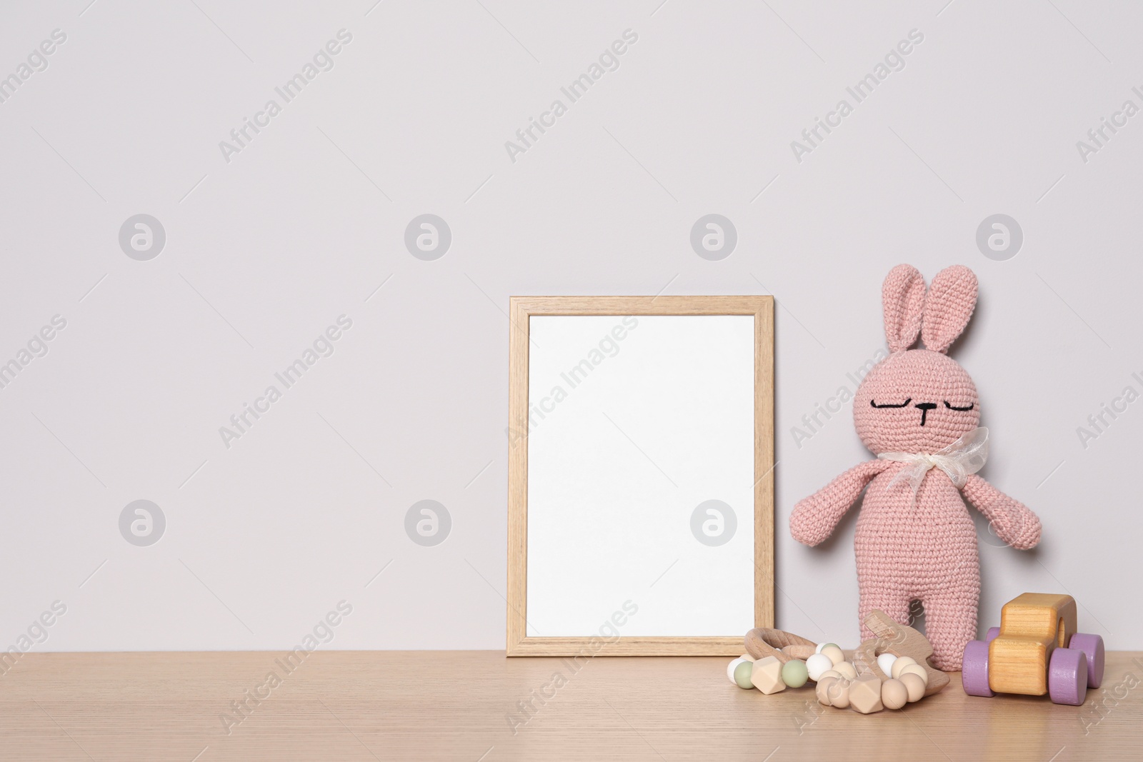 Photo of Empty square frame and different toys on wooden table, space for text