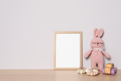 Photo of Empty square frame and different toys on wooden table, space for text