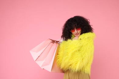 Happy young woman with shopping bags on pink background