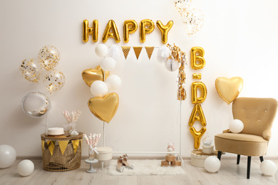 Photo of Phrase HAPPY BIRTHDAY made of golden balloon letters in decorated room