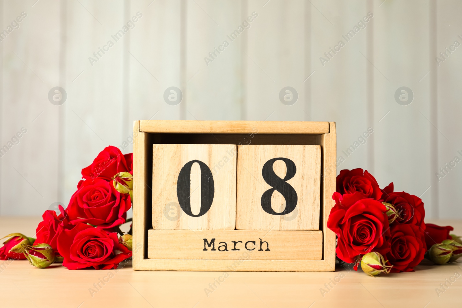 Photo of Wooden block calendar with date 8th of March and roses on table against light background, space for text. International Women's Day