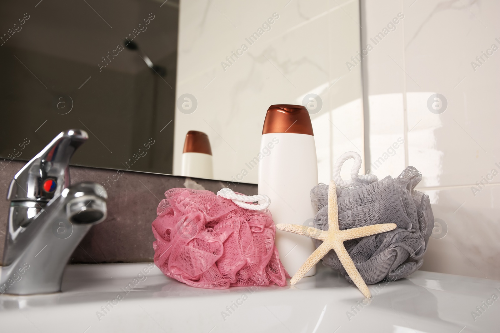 Photo of Colorful sponges between shower gel bottle and starfish on sink in bathroom