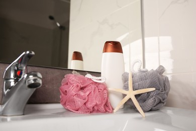 Colorful sponges between shower gel bottle and starfish on sink in bathroom