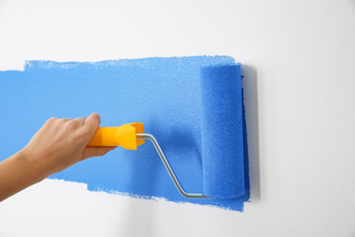 Photo of Woman painting white wall with blue dye, closeup. Interior renovation