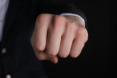 Photo of Businessman showing fist with space for tattoo on black background, closeup