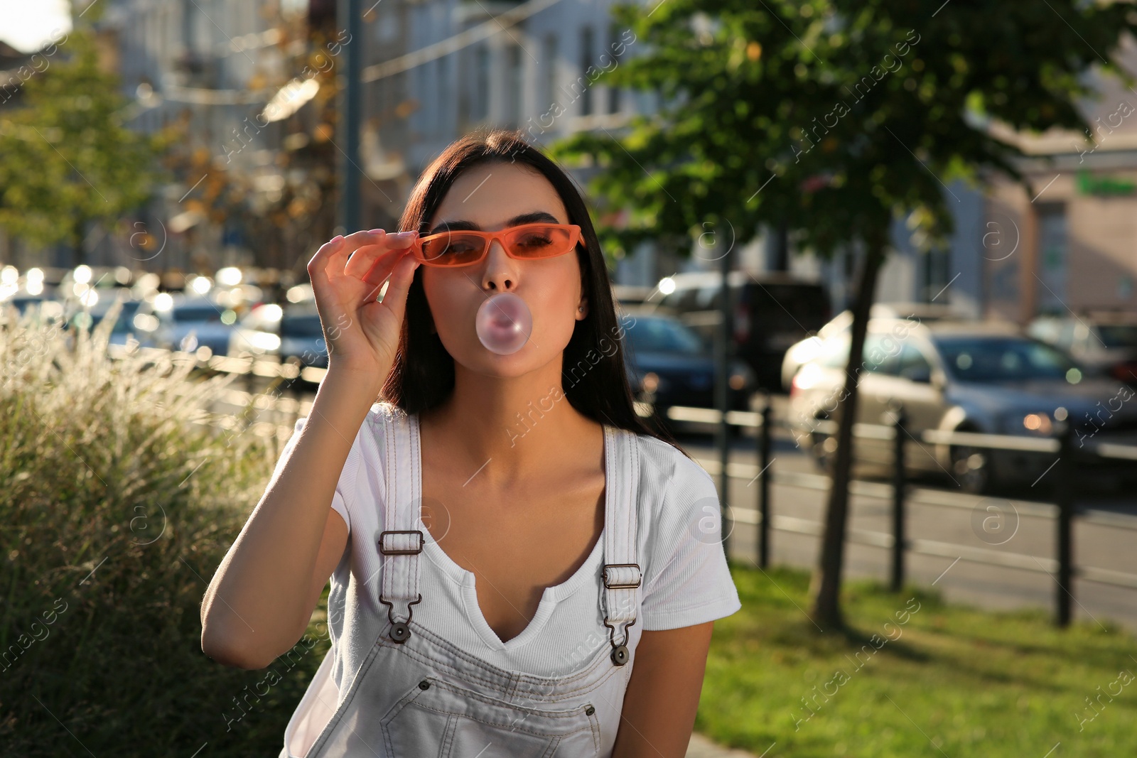 Photo of Beautiful woman in sunglasses blowing gum outdoors, space for text