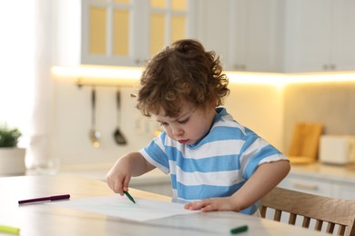 Photo of Cute little boy drawing with marker at table in kitchen